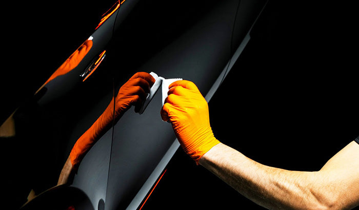 A man in orange gloves meticulously polishes a black car, showcasing professional car detailing and maintenance techniques.