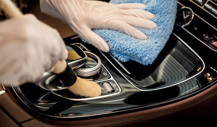 Person cleaning car interior with soft microfiber cloth, using tire seal spray on seats, rear window tint visible.