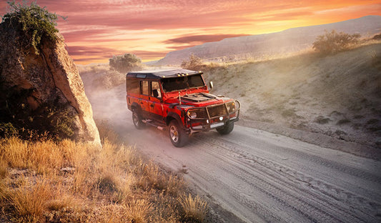 A red jeep driving down a dirt road at sunset. The image showcases a rugged vehicle amidst a scenic backdrop.